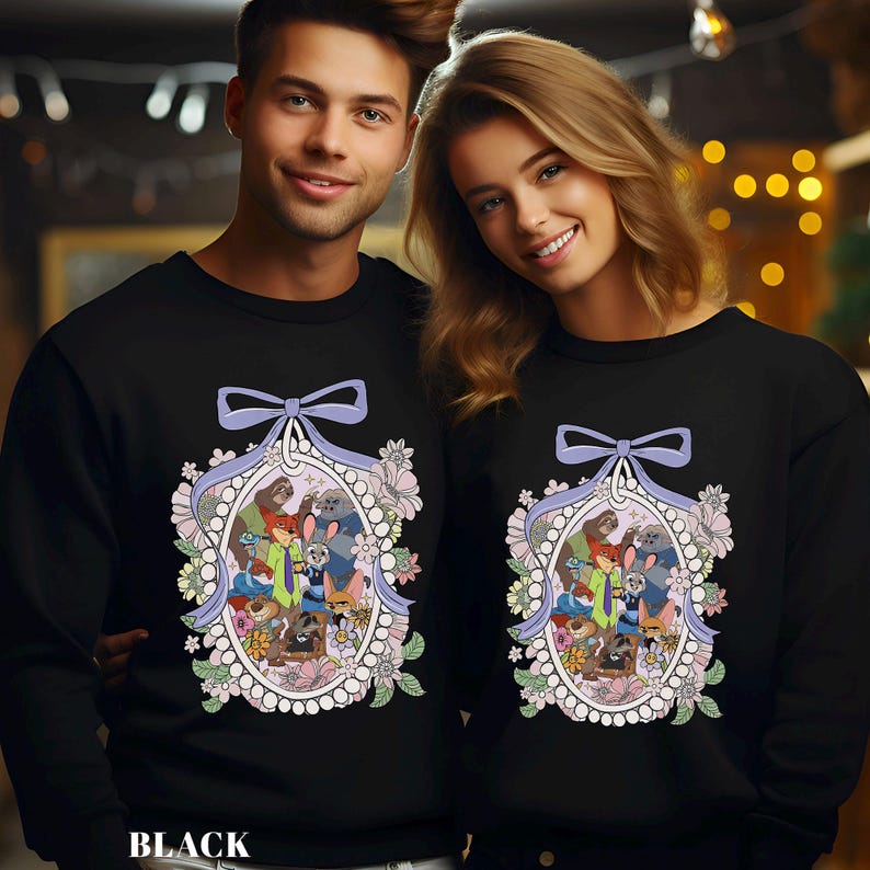 A man and a woman are standing next to each other, both wearing black sweatshirts with a colorful, whimsical design featuring cartoon characters and floral elements.