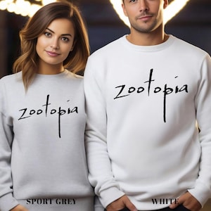 A man and a woman standing side by side, both wearing white sweatshirts with the word "Zootopia" printed on them.