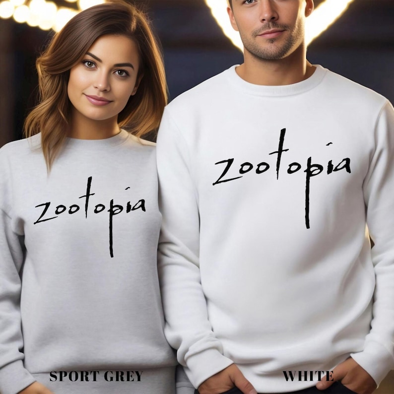 A man and a woman standing side by side, both wearing white sweatshirts with the word "Zootopia" printed on them.