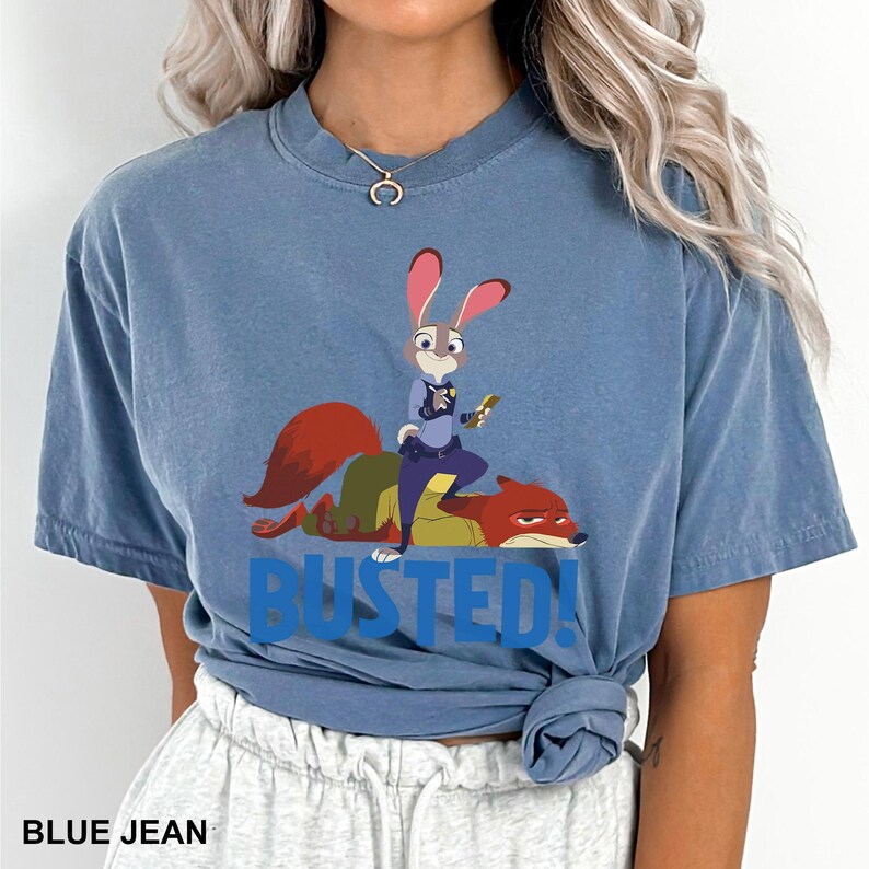 A woman wearing a blue t-shirt with a graphic of a cartoon rabbit character and the text "BUSTED!" printed on it.