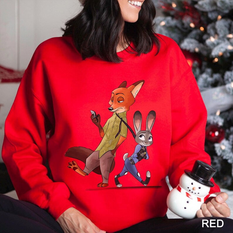 A woman wearing a red sweater with an illustration of a fox and a rabbit on it, holding a snowman.