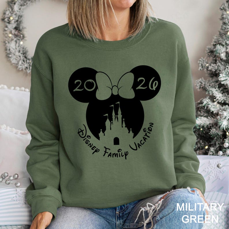 A woman wearing a green sweatshirt with a graphic design featuring a Minnie Mouse and a castle, along with the text "Disney Family Vacation".