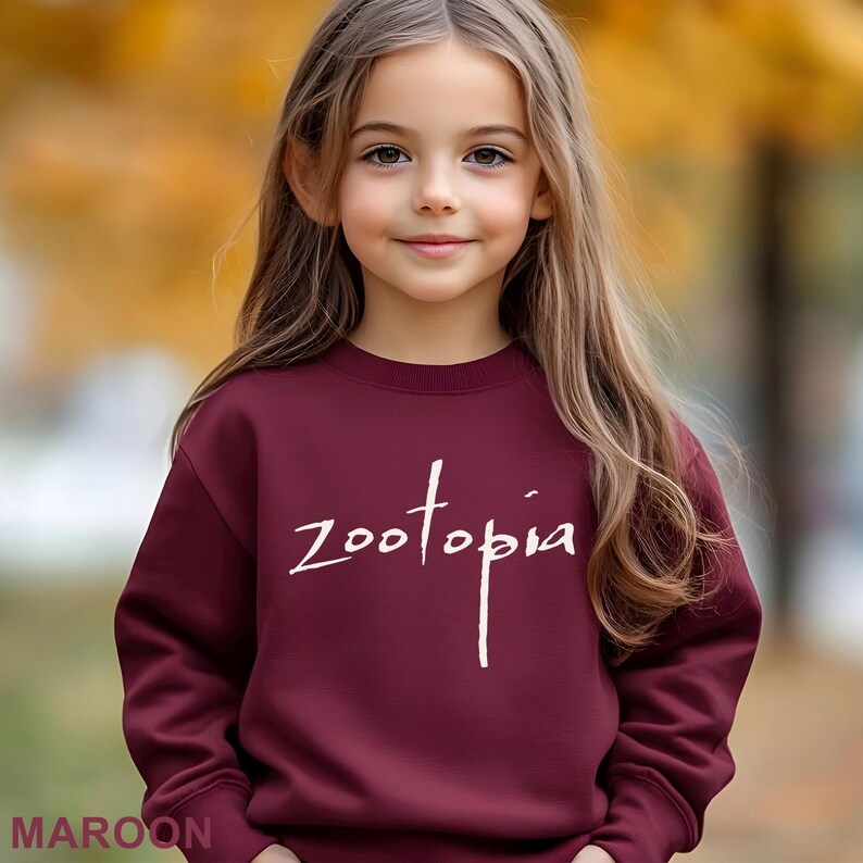 A young girl with long blonde hair wearing a maroon sweater with the word "Zootopia" printed on it.
