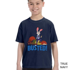 A young boy wearing a navy blue t-shirt with a cartoon rabbit character and the text "BUSTED!" printed on it.