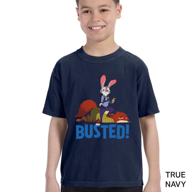 A young boy wearing a navy blue t-shirt with a cartoon rabbit character and the text "BUSTED!" printed on it.