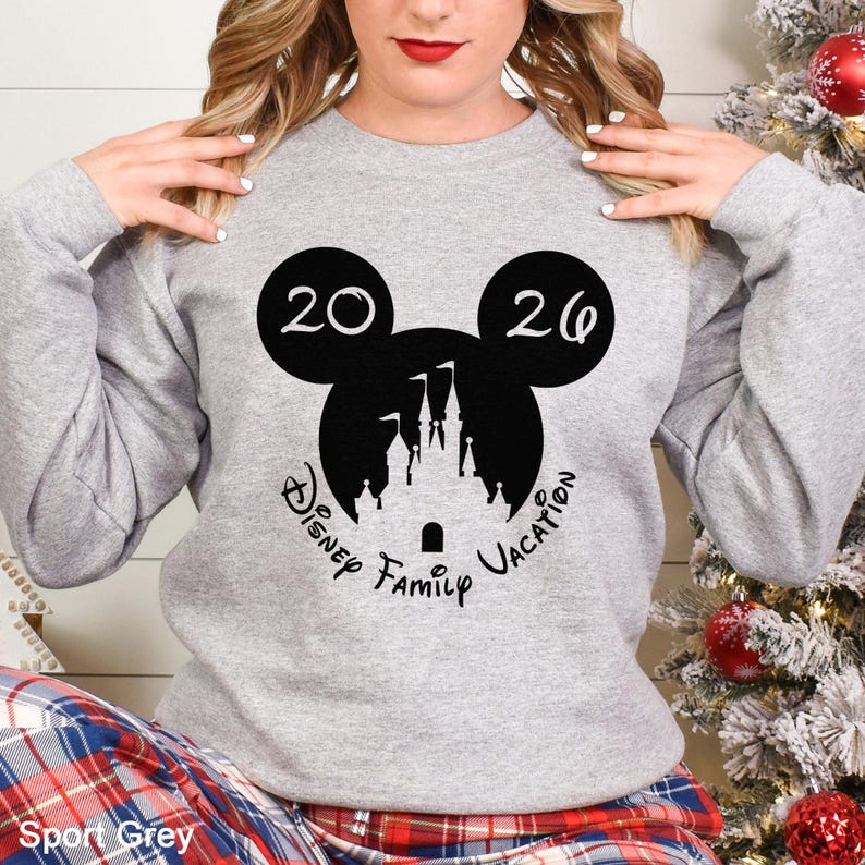 A woman wearing a gray sweatshirt with a Disney-themed graphic and text, posing in front of a Christmas tree.