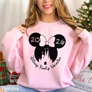 A woman wearing a pink sweatshirt with a Disney-themed design and the text "Disney Family Vacation" printed on it.