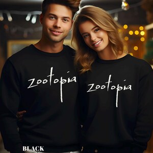 A man and a woman wearing black tops with the word "Zootopia" printed on them, smiling and posing together.