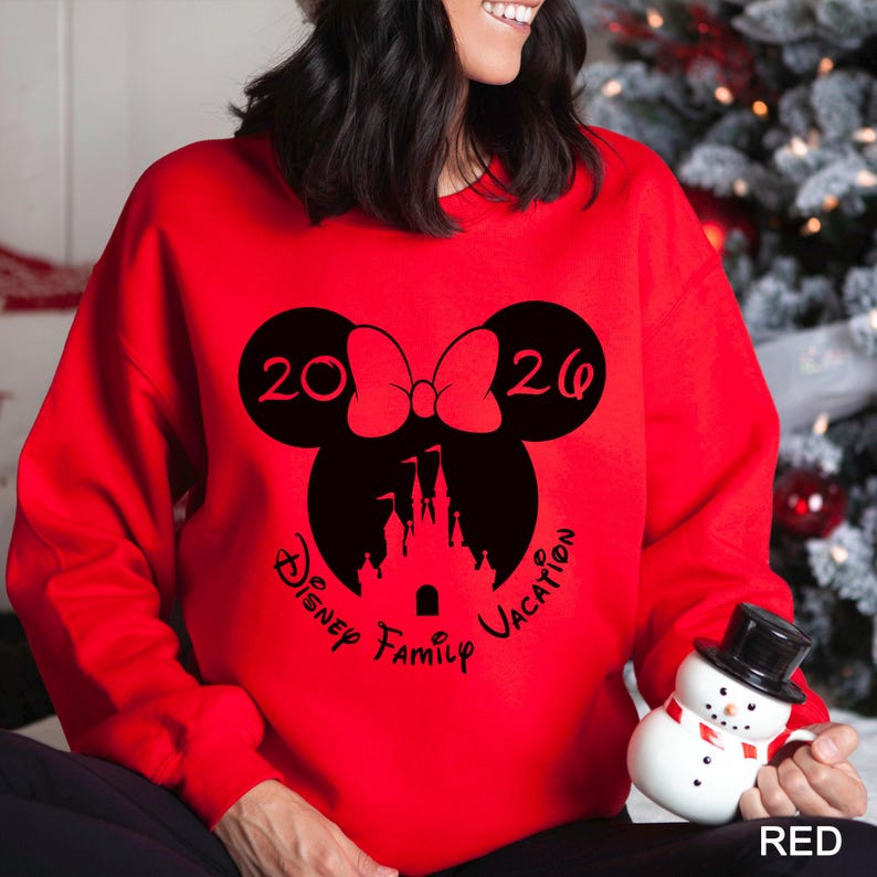A woman wearing a red sweater with a graphic design of a castle and the text "Disney Family Vacation" is holding a snowman and a mug.