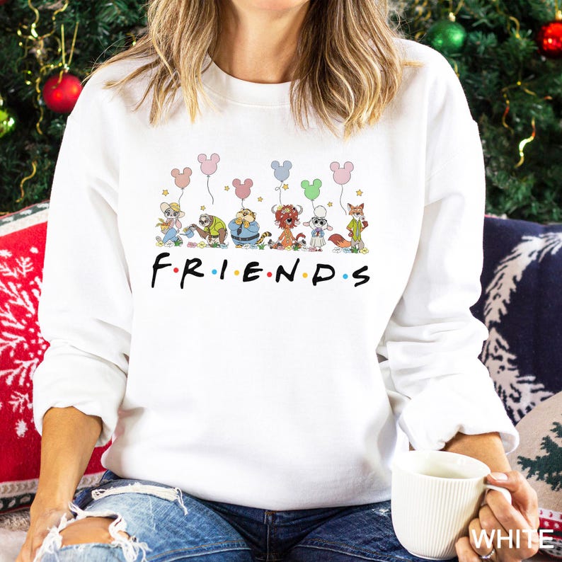 A woman wearing a white sweatshirt with a graphic of Disney characters and the word "FRIENDS" printed on it, sitting in front of a Christmas tree.