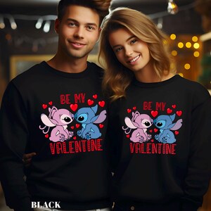 A man and a woman are standing next to each other, both wearing black sweatshirts with a Valentine's Day design featuring two cartoon characters.