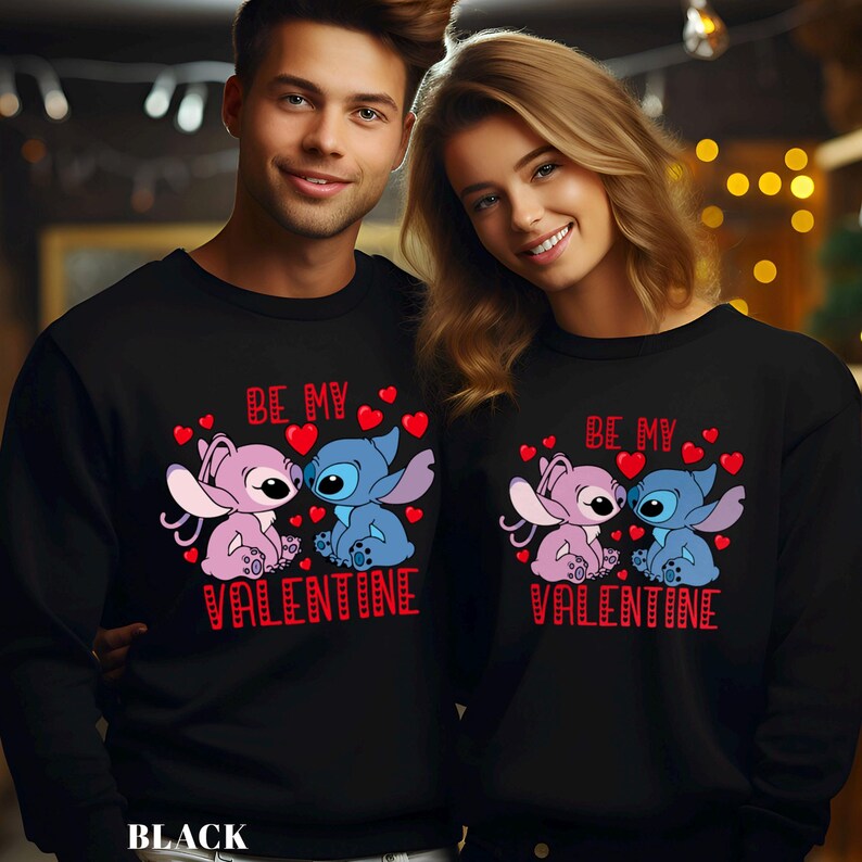 A man and a woman are standing next to each other, both wearing black sweatshirts with a Valentine's Day design featuring two cartoon characters.