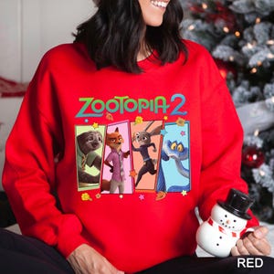A woman wearing a red sweater with a cartoon character design and holding a snowman.