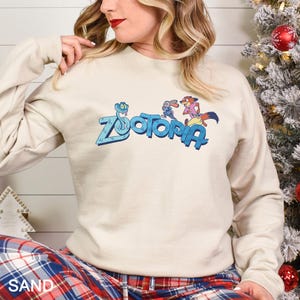 A woman wearing a white sweatshirt with the word "Zootopia" printed on it, sitting next to a Christmas tree.