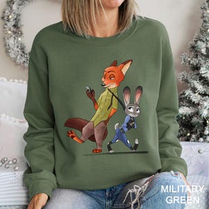 A woman wearing a green sweatshirt with an illustration of a fox and a rabbit character from the movie "Jurassic Park" on it.