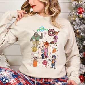 A woman wearing a white sweatshirt with a graphic of various cartoon animal characters, including a sloth, fox, and rabbit, along with other colorful and whimsical illustrations.