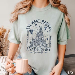 A woman wearing a t-shirt with a graphic design of a castle and stars, holding a cup of coffee.