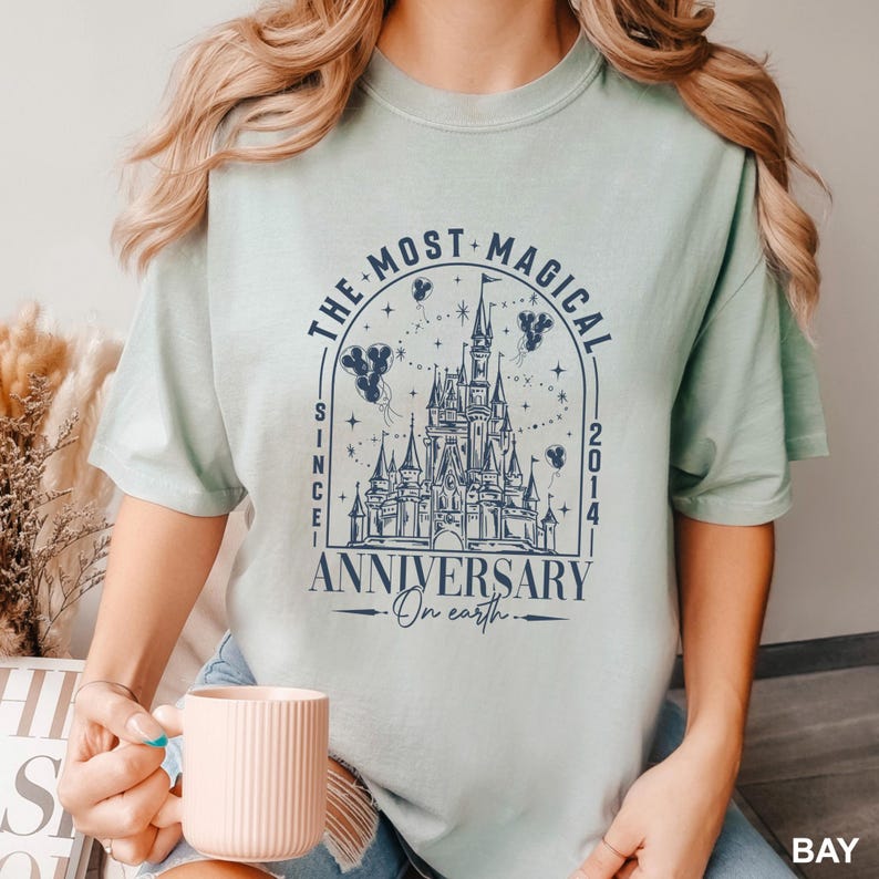 A woman wearing a t-shirt with a graphic design of a castle and stars, holding a cup of coffee.