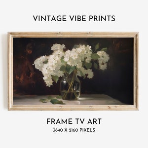 Könnte beinhalten: Ein Gemälde im Vintage-Stil mit einem Strauß weißer Blumen in einer klaren Glasvase auf einem weißen Tisch. Der Hintergrund ist dunkelbraun. Das Gemälde ist in einem hellen Holzrahmen gerahmt. "FRAME TV ART 3840 X 2160 PIXELS" ist unter dem Bild gedruckt.