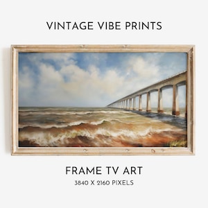 Op de afbeelding: Een ingelijste print van een lange brug die zich uitstrekt over een woelige zee onder een bewolkte hemel. Het kunstwerk bevindt zich in een houten lijst en bevat de tekst "VINTAGE VIBE PRINTS" en "FRAME TV ART". De beeldresolutie is 3840 x 2160 pixels.