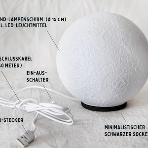 May include: A white, spherical lamp with a textured surface, resting on a black base. The lamp has a USB connector and a 1.40-meter cable. The text on the image says: "Moon lampshade (&Oslash; 15 cm) incl. LED light source".