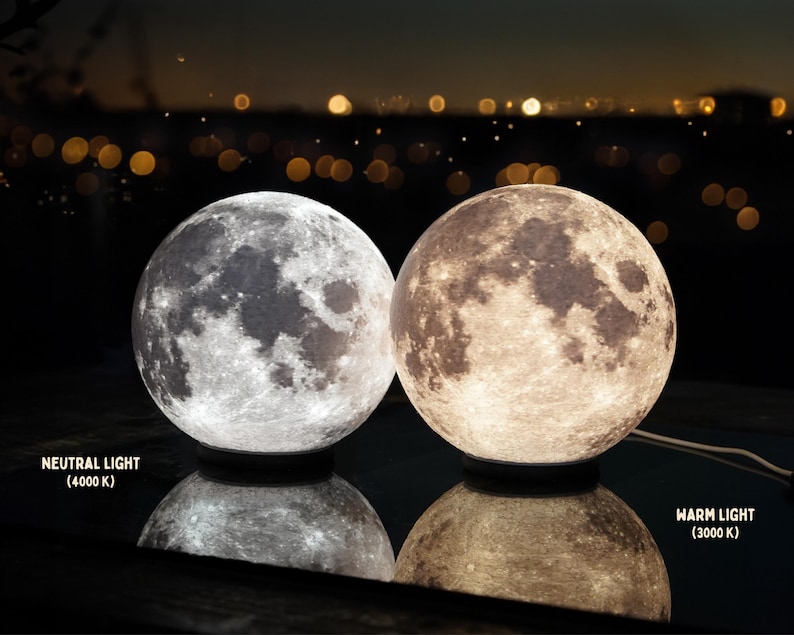 May include: Two spherical moon lamps, one with neutral light (4000 K) and the other with warm light (3000 K). The lamps are on a reflective surface, with the text "NEUTRAL LIGHT" and "WARM LIGHT" visible.