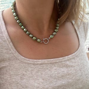 May include: A green pearl necklace with a silver clasp. The pearls are round and have a slight iridescent sheen.