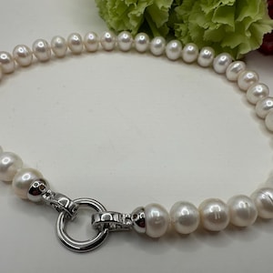 May include: A white pearl necklace with a silver clasp. The necklace is made of round pearls and has a simple design.