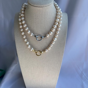 May include: Two-strand pearl necklace with a silver clasp and a gold clasp. The pearls are off-white and have a slightly irregular shape. The necklace is displayed on a beige mannequin.