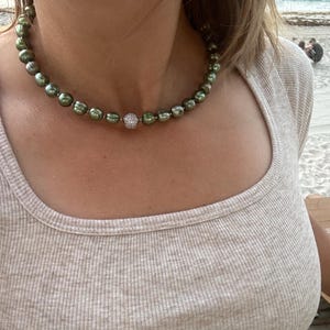May include: A green pearl necklace with a small, sparkly, round pendant.