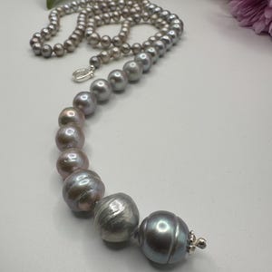 May include: A long strand of gray and lavender pearls with a large, iridescent pearl at the end. The pearls are strung on a silver chain.