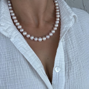 May include: A white shirt with a pearl necklace. The pearls are a light pink color.