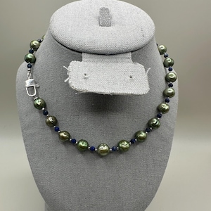 May include: A green and black pearl necklace with blue sapphire beads. The necklace is on a gray mannequin.