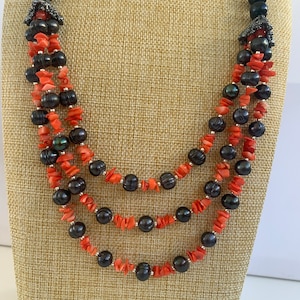 May include: A three-strand necklace with black pearls and orange coral beads.