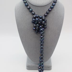 May include: A dark blue pearl necklace displayed on a gray mannequin. The necklace features a cluster of pearls at the center, with a long strand of pearls hanging down. The pearls have a lustrous sheen and are arranged in a classic style.