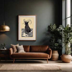 May include: A framed print of a black and white illustration of a goat with large horns standing in water. The print is titled "Capricorn" and is set against a dark green wall in a living room with a brown leather sofa and potted plants.