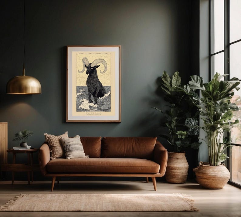 May include: A framed print of a black and white illustration of a goat with large horns standing in water. The print is titled "Capricorn" and is set against a dark green wall in a living room with a brown leather sofa and potted plants.