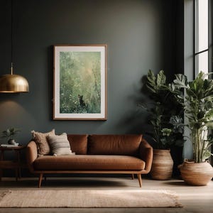 Może przedstawiać: Brązowa sk&oacute;rzana sofa z obrazem w ramie przedstawiającym leśną scenę wiszącym nad nią. Sofa znajduje się w pokoju z ciemnozielonymi ścianami i dużym oknem. W pokoju znajdują się dwie rośliny doniczkowe, jedna z zielonymi liśćmi, a druga z dużymi, ciemnozielonymi liśćmi.