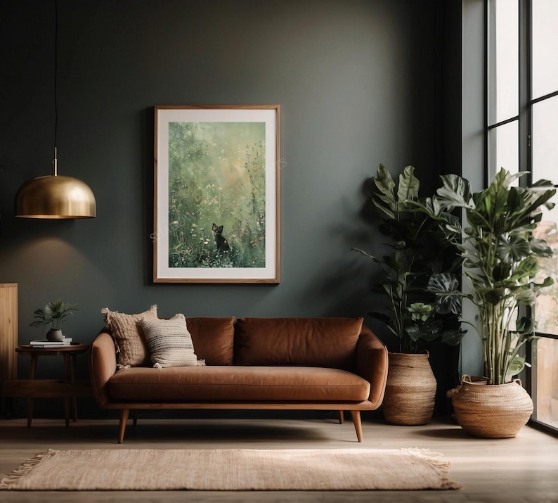 Może przedstawiać: Brązowa sk&oacute;rzana sofa z obrazem w ramie przedstawiającym leśną scenę wiszącym nad nią. Sofa znajduje się w pokoju z ciemnozielonymi ścianami i dużym oknem. W pokoju znajdują się dwie rośliny doniczkowe, jedna z zielonymi liśćmi, a druga z dużymi, ciemnozielonymi liśćmi.