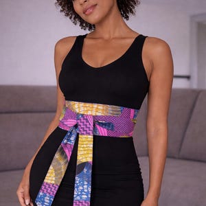Puede incluir: Un vestido negro con un cintur&oacute;n estampado colorido. El cintur&oacute;n presenta una mezcla de dise&ntilde;os geom&eacute;tricos y abstractos rosas, amarillos y azules. El vestido tiene un escote en V.