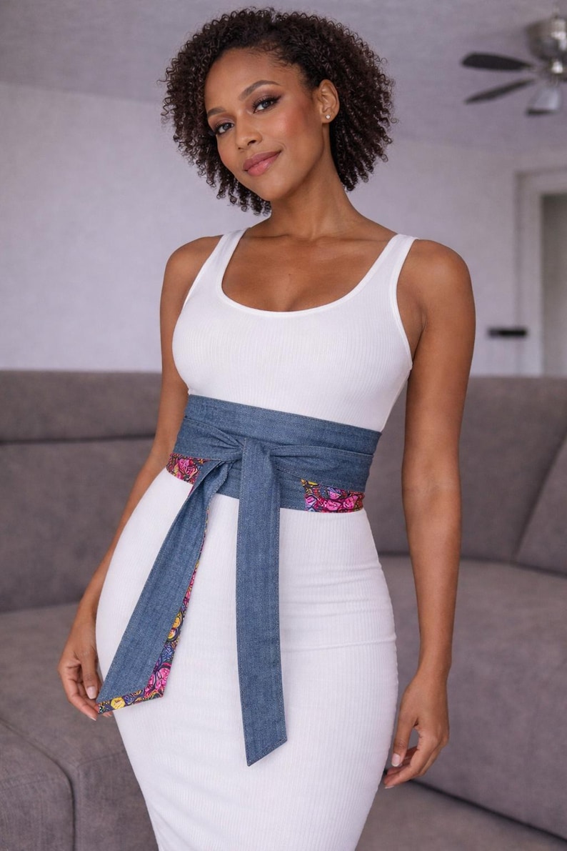 Puede incluir: Una mujer con un vestido blanco de tirantes acanalado y un cintur&oacute;n envolvente de mezclilla. El cintur&oacute;n tiene un forro con estampado floral. El vestido es entallado. El cintur&oacute;n est&aacute; atado con un lazo en la cintura.