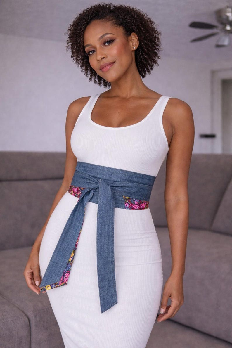 Puede incluir: Una mujer con un vestido blanco de tirantes acanalado y un cintur&oacute;n envolvente de mezclilla. El cintur&oacute;n tiene un forro con estampado floral. El vestido es entallado. El cintur&oacute;n est&aacute; atado con un lazo en la cintura.