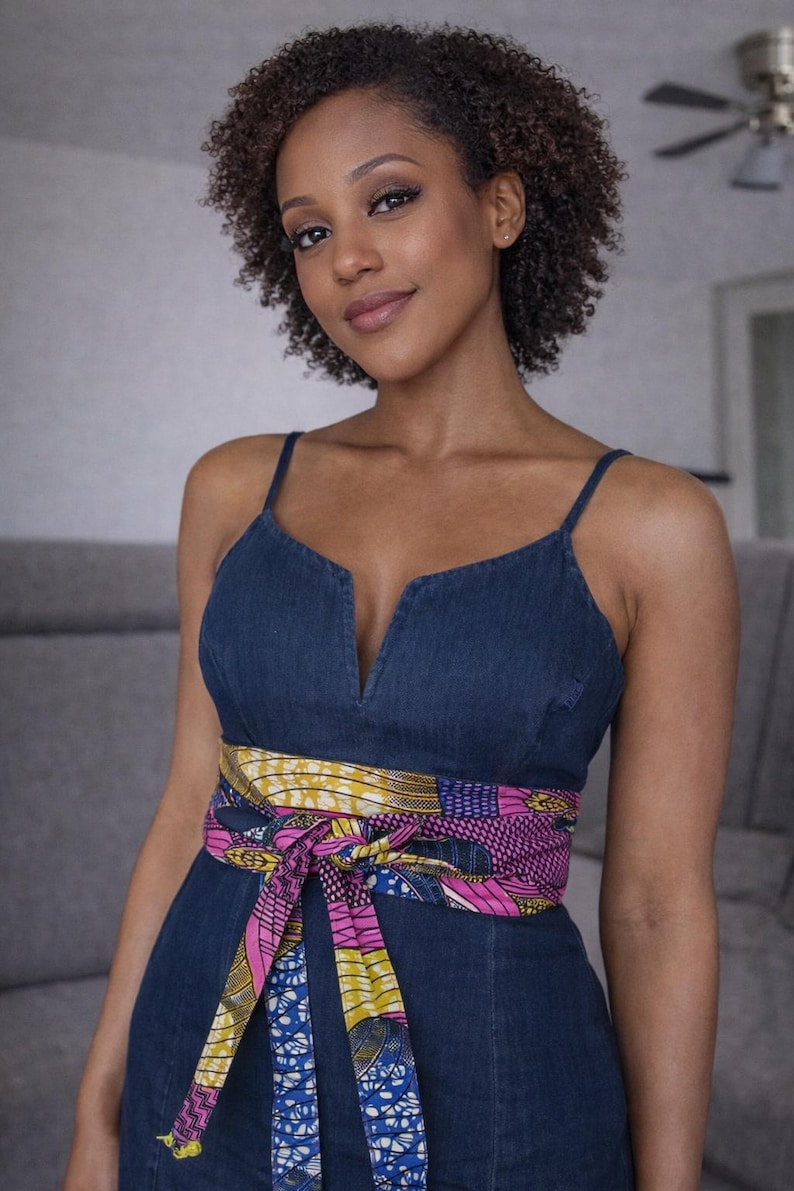 Puede incluir: Vestido vaquero azul oscuro con tirantes finos y escote en V. La cintura se ci&ntilde;e con un cintur&oacute;n estampado colorido con tonos rosas, amarillos y azules. El vestido es de color azul oscuro.
