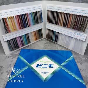 Puede incluir: Muestras de hilo de varios colores, dispuestas en tarjetas blancas con escalas numeradas. Una caja azul con texto japonés y la inscripción "POLYESTER 100%" está en primer plano. El logotipo de KESTREL SUPPLY es visible.