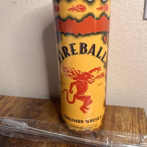 May include: A yellow and red Fireball Cinnamon Whisky tumbler with a red lid. The tumbler features the Fireball logo, a red devil, and the words "Cinnamon Whisky". A stainless steel straw and brush are included.