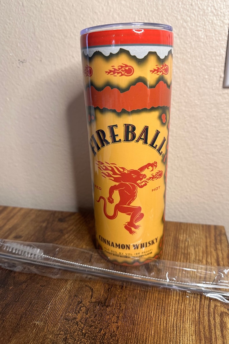 May include: A yellow and red Fireball Cinnamon Whisky tumbler with a red lid. The tumbler features the Fireball logo, a red devil, and the words "Cinnamon Whisky". A stainless steel straw and brush are included.