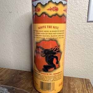 May include: A cylindrical tumbler with a clear lid, featuring a fiery design and the text "IGNITE THE NITE." The tumbler has a yellow background with orange flames and a silhouette of a figure. The text describes the drink as smooth whisky with cinnamon.