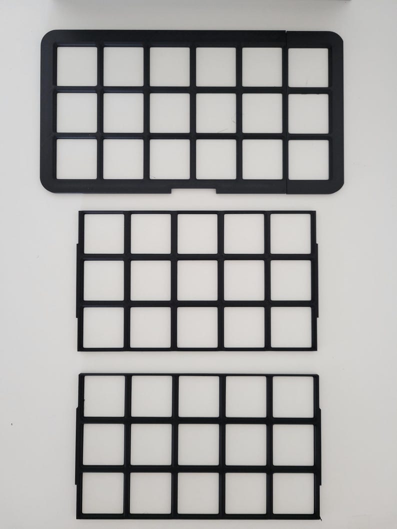 May include: Three black rectangular grid organizers with a uniform square pattern. The top piece features a solid outer frame with rounded corners, while the two lower pieces consist of thin, open-frame dividers with small side tabs for assembly.