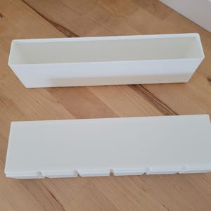 May include: Two rectangular, white planters are displayed on a wooden surface. One planter is open, while the other has a lid with four cut-out sections. The planters are designed for indoor or outdoor use.