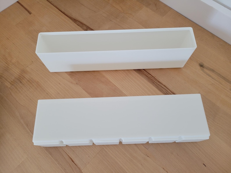 May include: Two rectangular, white planters are displayed on a wooden surface. One planter is open, while the other has a lid with four cut-out sections. The planters are designed for indoor or outdoor use.